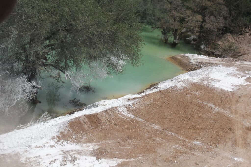 Contaminación visible en el Río Sonora, con aguas turquesa y sedimentos en la orilla, reflejando el impacto del derrame de Grupo México.