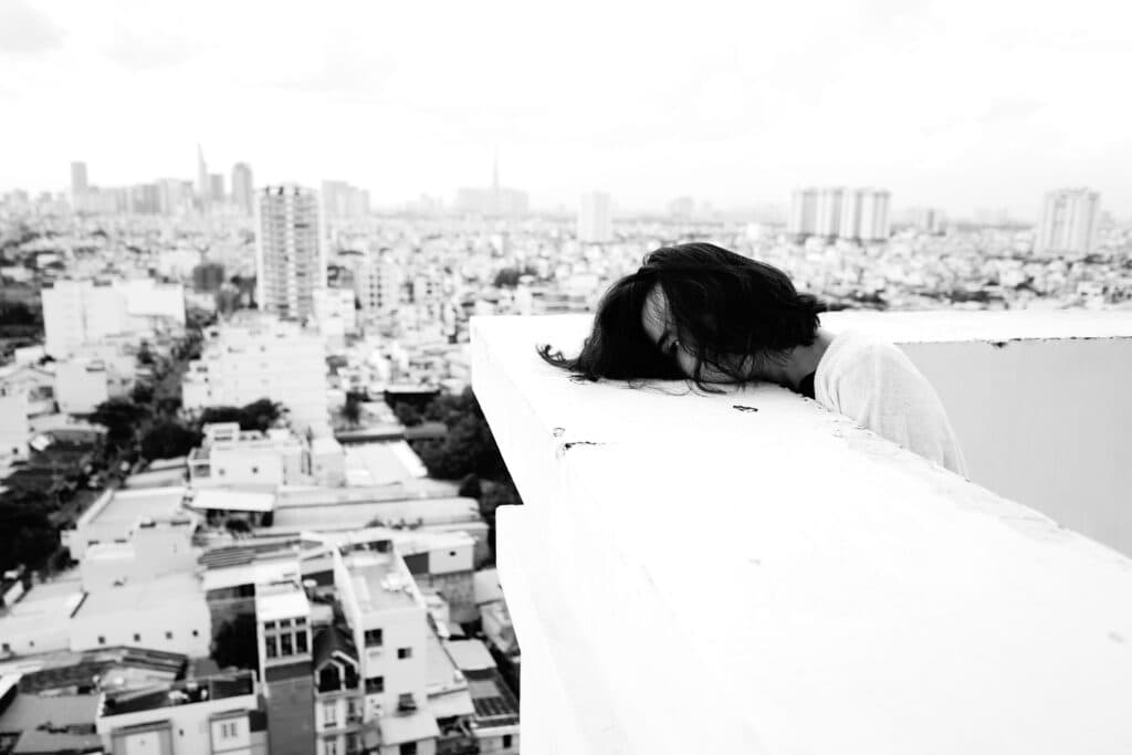 Persona con cabello largo agachada sobre un borde en un edificio alto, con vista a una ciudad. Refleja la crisis de salud mental en México.