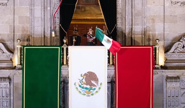 Claudia Sheinbaum en el balcón de Palacio Nacional, ondeando la bandera mexicana, durante el Grito de Independencia en el Zócalo.